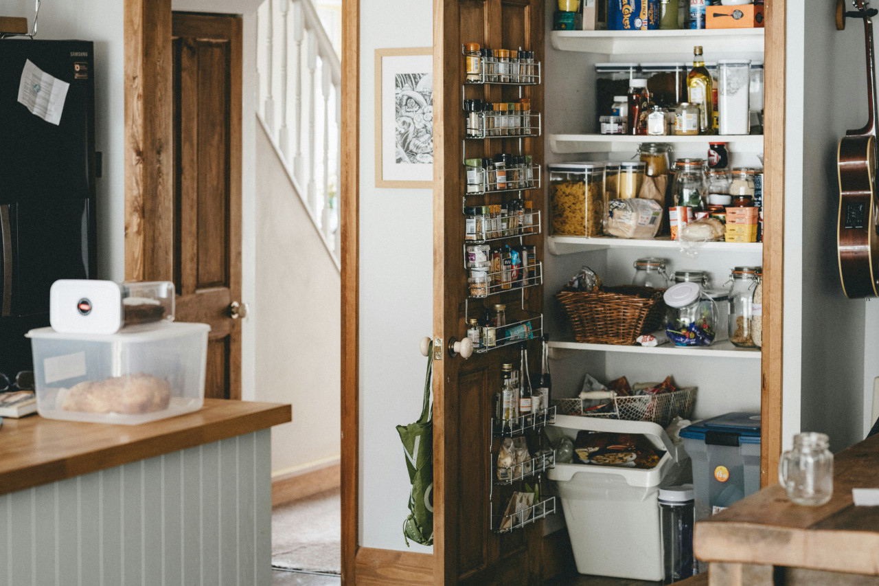 An Organized Kitchen Pantry Stocked With Food; The Pantry Has a Spice Rack Door Organizer Plus Space for Storing Small Appliances  and Trash Cans for Keeping the Kitchen Looking Clutter-Free. Photo Courtesy of Annie Spratt 